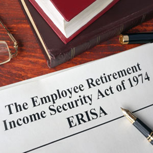 Document titled "The Employee Retirement Income Security Act of 1974" (ERISA), with a pen, glasses, and a book on a wooden table